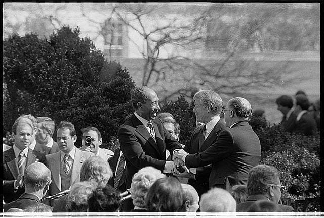 Sadat, Carter and Begin seated at a long table on the White House lawn signing the Egypt-Israel peace treaty in March 1979.
