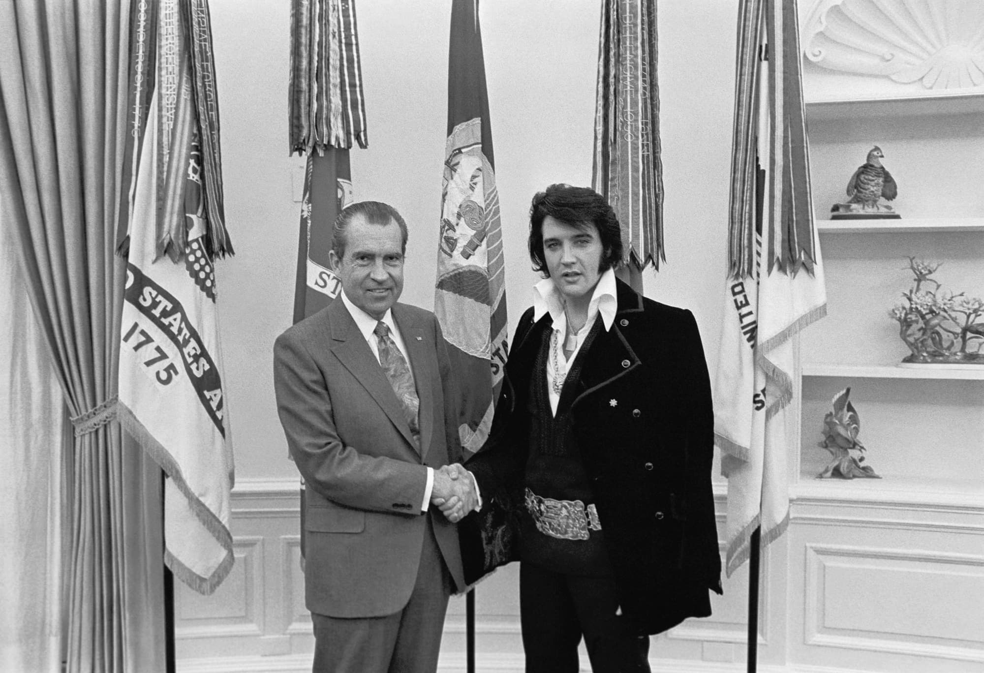 Elvis Presley shaking hands with Richard Nixon in the Oval Office, Presley in a caped velvet suit with a large belt buckle.