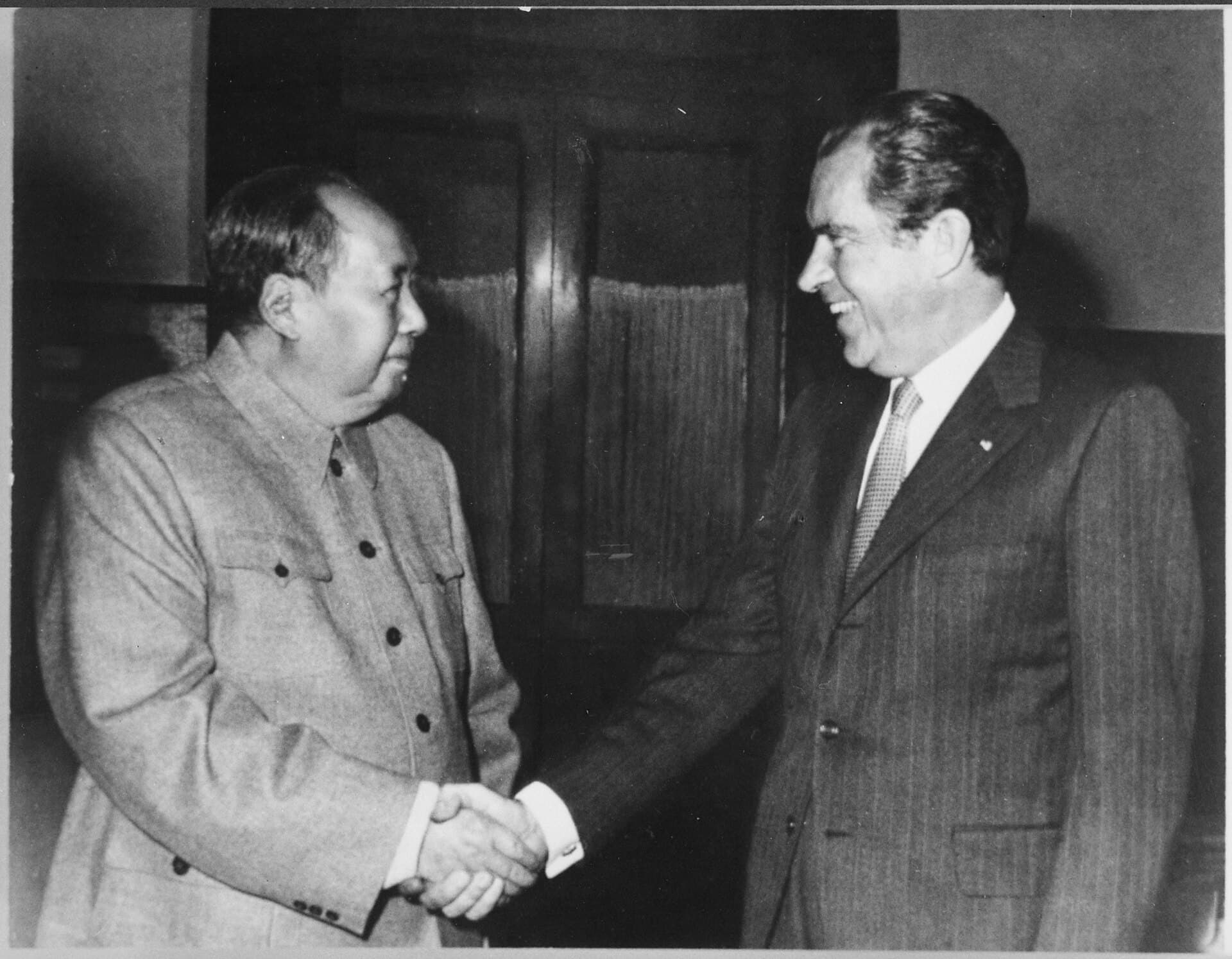 President Richard Nixon and Chairman Mao Zedong shaking hands in Mao's study in Beijing, surrounded by bookshelves, February 1972.