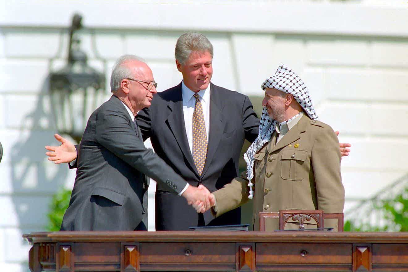 Yitzhak Rabin and Yasser Arafat shaking hands on the White House lawn with Bill Clinton standing between them.